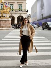 a lady wears a classic trench coat with a white blouse and black pants